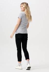 Grå kortærmet t-shirt parret med sorte tætsiddende bukser og hvide sportsko. Modellen er vendt lidt, så der vises et sideview.
