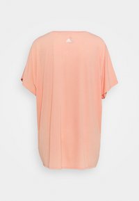 Lyserød oversized t-shirt med rund halsudskæring og korte ærmer. Har et lille hvidt Adidas-logo på ryggen. Blød, glat tekstur.