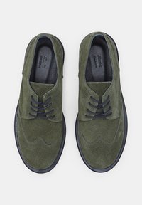 Pantofi din suede verde închis, cu vârful rotunjit și cusături decorative. Au șireturi întunecate și o talpă din cauciuc negru în contrast.