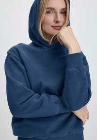 Felpa con cappuccio blu navy in un materiale morbido, dotata di polsini e orlo a coste, con una vestibilità rilassata e dettagli di design minimi.