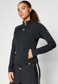 Juodas sportinis džemperis su aukštu apykakle, pilnai užtraukiamos priekio užtrauktuku, užtraukiamomis kišenėmis ir tekstūruotu audiniu. Ant rankovės yra logotipas.