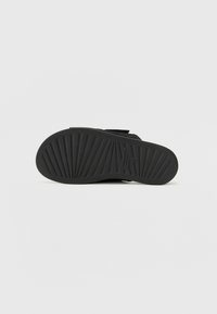 Black sandal with a textured rubber sole featuring horizontal ridges; includes adjustable straps for a secure fit.