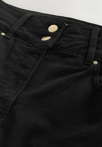 Gros plan sur un jean en denim noir avec deux boutons dorés et des passants de ceinture à la taille.