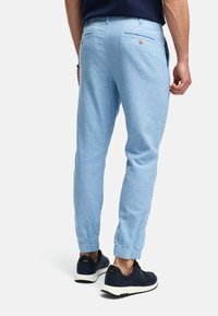 Pantalones de chándal de color azul claro, con corte ajustado y puños elásticos, bolsillos traseros con botones y textura de tela suave. Llevados con zapatillas de deporte marinas.