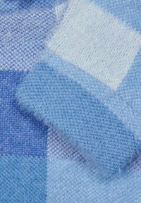 Gewebter blauer Pulloverstoff mit weicher Textur, unterschiedlichen Blautönen und einem flauschigen weißen Fleck, der ein kariertes Muster erzeugt.