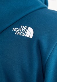 Gros plan sur un vêtement bleu avec le logo blanc The North Face imprimé sur le haut de la poitrine.