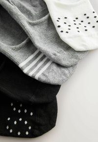 Quatre paires de chaussettes basses en blanc à pois noirs, gris clair à rayures, gris uni, et noir uni à pois blancs.