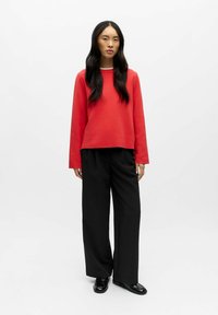 Punane pika varrukaga ja ümarakaelusega dressipluus, kombineeritud mustade laia säärega pükstega. Sile tekstuur, moodne lõige, minimaalne detailide kasutus.