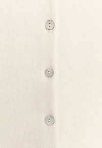 Krémově zbarvený pletený cardigan s texturovaným povrchem, s čtyřmi kulatými, perleťovými knoflíky po celé délce přední části. Jednoduchý a hladký design.