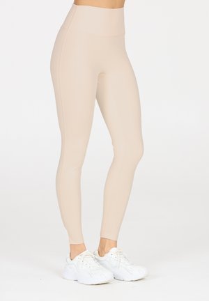 Leggings beiges taille haute en matière extensible, avec un design épuré et une coupe étroite. Associés à des baskets de sport blanches.