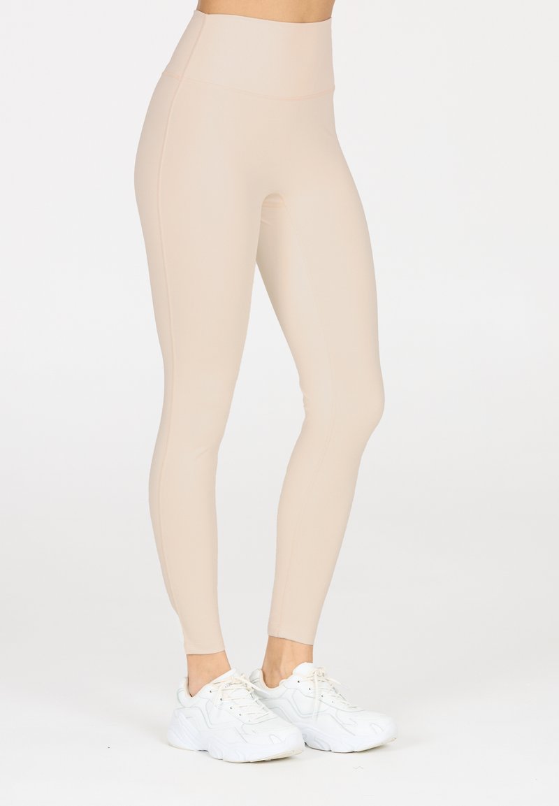 Leggings beige a vita alta realizzati in materiale elastico, con un design elegante e una vestibilità slim. Abbinati a sneakers sportive bianche.