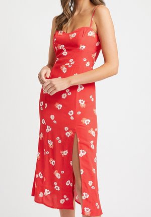 Rød midi kjole med hvidt og ferskenfarvet blomsterprint, tynde stropper, tætsiddende korset og sideslids, båret af en kvinde med løst hår.