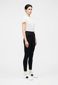 Leggings neri a vita alta abbinati a una maglietta bianca a maniche corte e sneaker bianche con un dettaglio nero. Design liscio e aderente.
