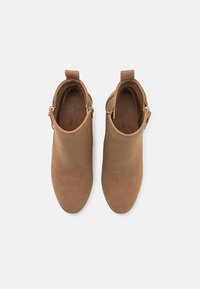 Brown vegan ankle boots with a smooth texture, rounded toe, and side zipper. Features a small pull tab at the back for easy wear.