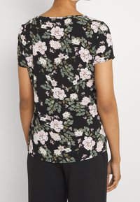 Svart blommig kortärmad topp med stora rosa och vita blommor samt gröna blad, rund halsringning och böjd fåll. Slät tygtextur.