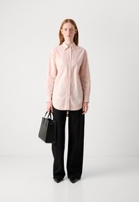 Light pink button-up shirt with long sleeves, paired with black wide-leg pants featuring subtle sparkles, held with a small black handbag.