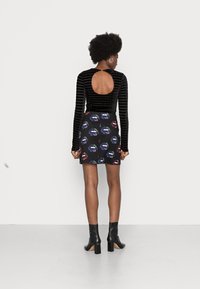 Top de veludo preto de mangas longas com um recorte nas costas, combinado com uma saia mini estampada com lábios coloridos sobre um fundo preto. Botas pretas de salto alto.