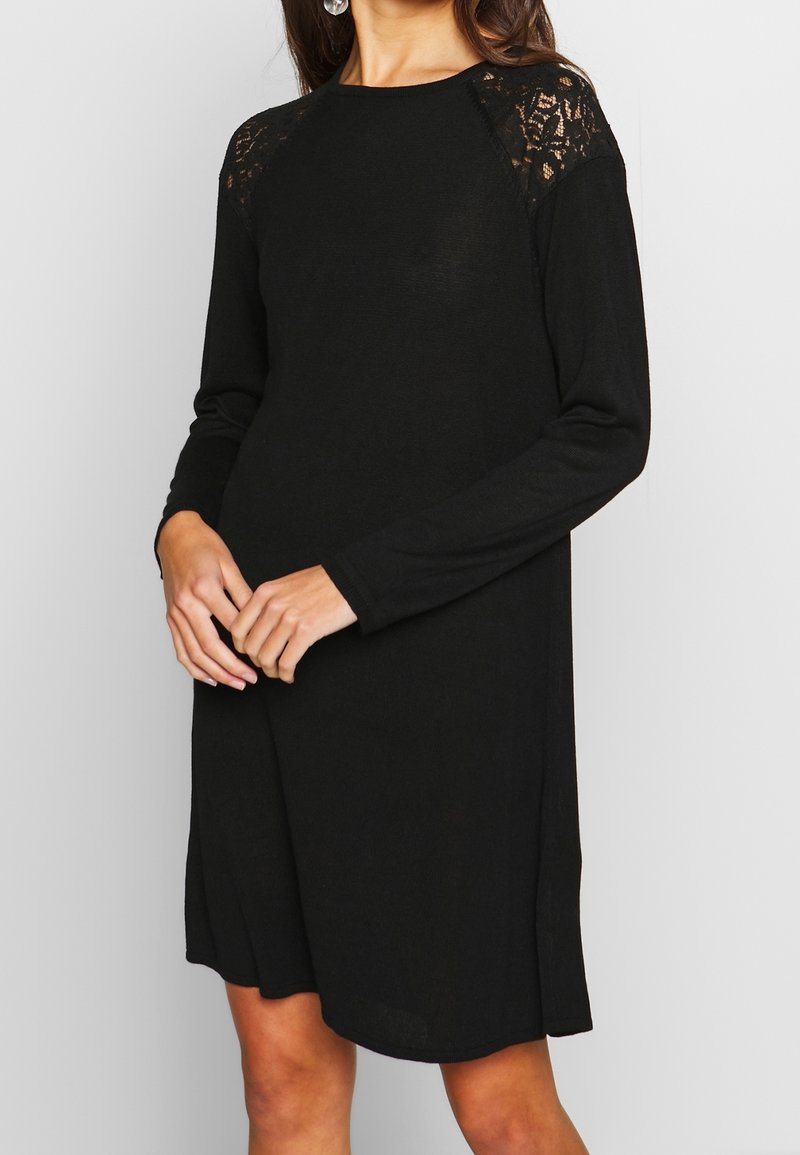 Vestito nero a maniche lunghe con dettagli in pizzo sulle spalle, caratterizzato da una vestibilità comoda e una texture morbida. Collo rotondo semplice, lunghezza al ginocchio.