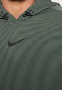 Gros plan sur un sweat à capuche vert côtelé avec le logo Nike Swoosh noir et des cordons de serrage ajustables près du cou.