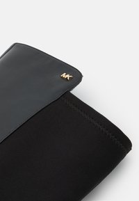 Gros plan d'un cuissard noir avec garniture en cuir et logo doré MK, présentant des coutures en zigzag sur la partie en tissu.