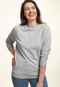 Felpa grigia con maniche lunghe, collo rotondo e polsini a costine. Tessuto morbido e strutturato, vestibilità rilassata, indossata con jeans blu.