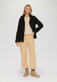 Schwarzer Knopfverschlussmantel, beiger gestreifter Pullover, hellbeige Cordhose, beigefarbene Schnürstiefel. Einfaches Design und neutrale Farbpalette.