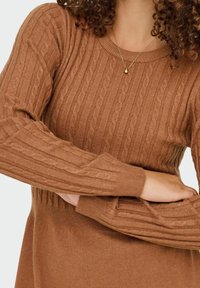 Rjav pulover pletenke z ribasto teksturo, okroglim izrezom in dolgimi rokavi. Značilno za svoj mehak material in topl ton.