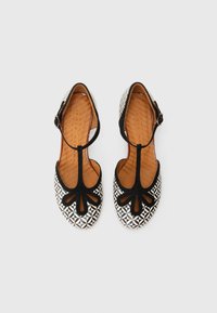 Κλειστά παπούτσια σε μαύρο και λευκό με σχέδιο, διαθέτουν λουράκι Τ και ρυθμιζόμενο πόρπη. Φέρουν γεωμετρικό σχέδιο και εσωτερική σόλα από δέρμα με υφή.