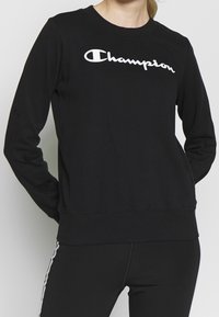 Zwarte sweatshirt van katoenmix, voorzien van een wit "Champion" logo, klassieke ronde halslijn en geribbelde boorden en zoom.
