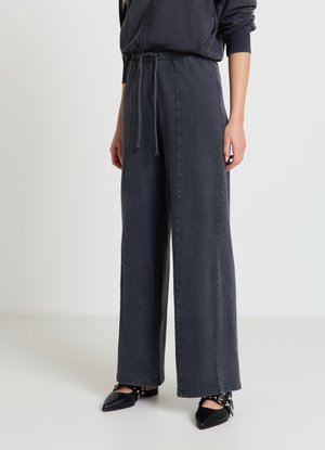 Weit geschnittene Hosen aus dunkelgrauem Denim mit elastischem Kordelzugbund. Sie zeichnen sich durch eine lässige Passform und ein minimalistisches Design aus, kombiniert mit schwarzen spitzen Schuhen.