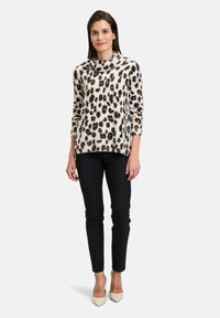Cremefarbener Pullover mit Kapuze, versehen mit einem schwarz-braunen Leopardenmuster, kombiniert mit schwarzen, enganliegenden Hosen und beigen High Heels.