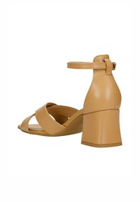 Braune Leder-High-Heelsandalen mit einem Knöchelriemen, die an der Vorderseite gekreuzte Riemen und einen klobigen Absatz haben. Glatte Textur und minimalistisches Design.
