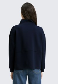 Pull bleu marine avec un col montant, des épaules tombantes et une coupe décontractée. Fabriqué en tissu doux avec une texture subtile et une couture au dos.