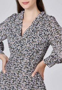 Robe portefeuille florale avec un décolleté en V profond, fond marine et motifs de petites fleurs multicolores. Manches longues avec des détails froncés.