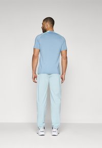 Lyseblå kortermet t-skjorte og lyseblå joggebukser med elastiske mansjetter, sammen med hvite joggesko, sett bakfra mot en ensfarget bakgrunn.