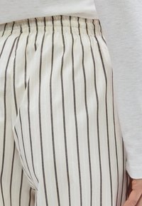 Pantalon en mélange de coton avec une base beige clair ornée de fines rayures verticales marron, taille élastique et texture lisse.