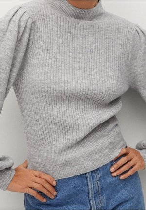 Pull gris côtelé avec des épaules bouffantes, porté avec un jean denim bleu, mains posées sur les hanches.