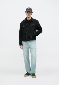 Μαύρο τζιν μπουφάν με δύο τσέπες στο στήθος, σε συνδυασμό με ανοιχτό μπλε τζιν και πράσινα αθλητικά παπούτσια. Το μοντέλο φορά γκρι καπέλο.