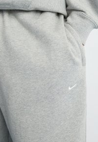 Šedé bavlnené tepláky s mäkkou textúrou, so bočnou vreckom a malým bielym logom Nike pri páse.