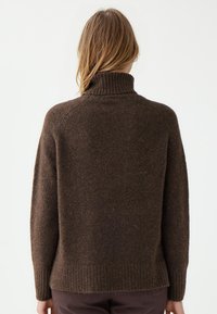 Bruine, zachte wollen trui met een hoge ribbels kraag, raglanmouwen en een ruime pasvorm. Heeft ribbelboorden en een iets langere achterkant.
