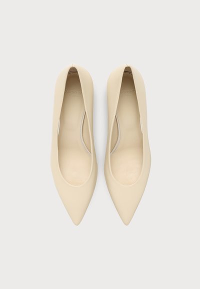 Paire de chaussures plates beige à bout pointu vues de dessus sur fond blanc.