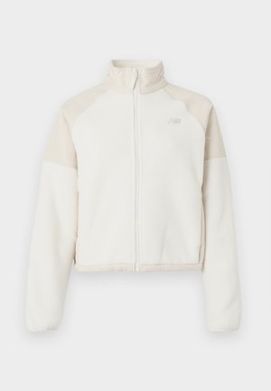 Przycięta kurtka polarowa w kolorze off-white z jasnobeżowymi akcentami, z pełnym zamkiem, wysokim kołnierzem i haftowanym logo na klatce piersiowej. Miękka faktura.