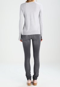 Szary dopasowany sweter z długimi rękawami, zestawiony z ciemnoszarymi obcisłymi jeansami. Charakteryzuje się prążkowanym dołem i prostymi tylnymi kieszeniami. Jasne tło.