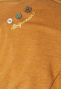 Mustard yellow sweater with a textured finish, featuring three decorative buttons and embroidered "dagwear" in gold.