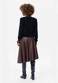 Czarny sweter prążkowany zestawiony z brązową skórzaną spódnicą w kształcie litery A oraz czarnymi botkami na obcasie do kolan, charakteryzującymi się gładką fakturą i dopasowanym krojem.