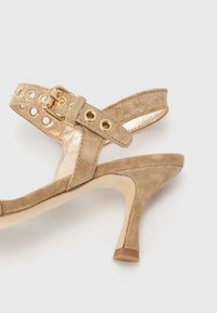 Beige Wildleder-Peeptoe-Sandale mit einem Riemen, der über goldene Beschläge und Aussparungen verfügt, strukturiertem Obermaterial und einem konischen Absatz.
