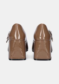 Zapatos de tacón bloque de charol marrón con un acabado suave. Incluyen un lazo decorativo y un detalle de cremallera en el lateral.