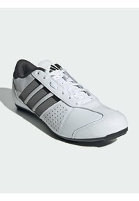 Bílé a šedé sportovní tenisky s černými pruhy, bílými tkaničkami, perforovanou boční částí a polstrovaným černým límcem na pozadí bílé barvy.