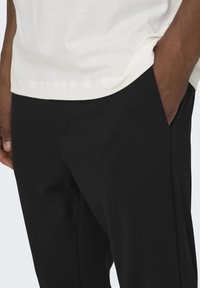 Zwarte broek met een gladde textuur, voorzien van een zijzak en een getailleerd ontwerp. Combineert met een lichtgekleurde blouse met een ronde zoom.