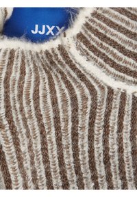 Gros plan sur le col d'un pull en tricot rayé marron et blanc avec une étiquette bleue visible affichant une partie du nom de la marque JJXX.